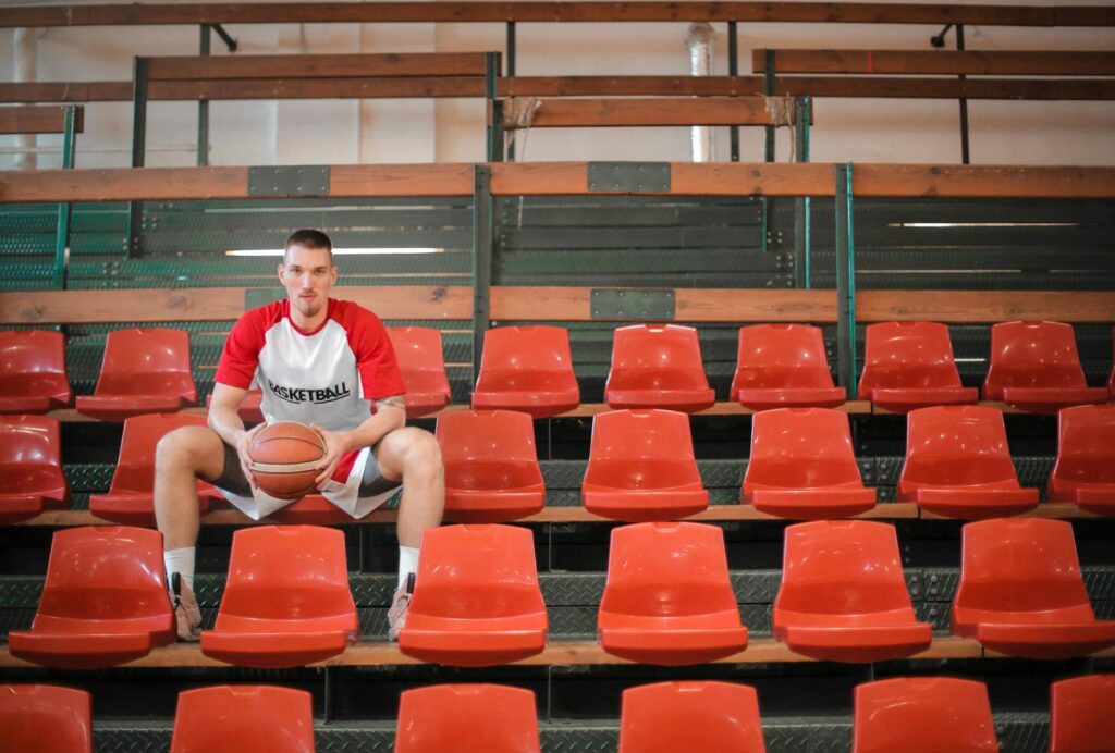 photo by andrea piacquadio Young basketball player sitting confidently in empty indoor stadium bleachers holding a ball.